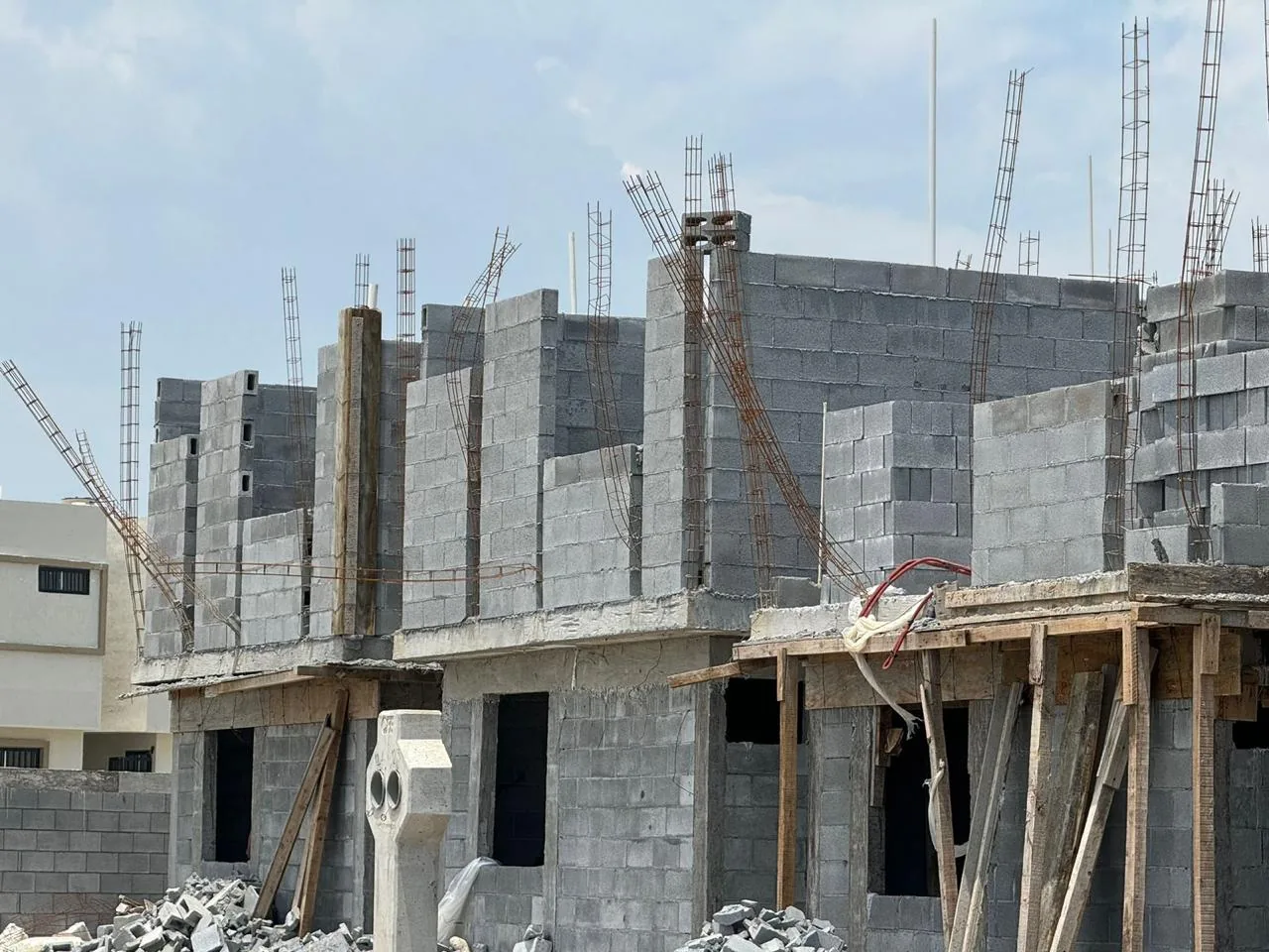 Conjunto de viviendas en construcción con muros de block, varilla y estructura habitacional en proceso.